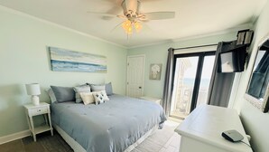 A bedroom with a bed, nightstand, and desk. There is a ceiling fan, a window with curtains, and a view of the outdoors. - Top floor Oceanfront Cherry Grove, North Myrtle Beach, SC 2 Bed 2 Bath Sleeps 7! (North Myrtle Beach)