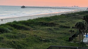 A beach with a wooden pier extending into the ocean, grassy areas, and a wooden staircase leading down to the beach. - Top floor Oceanfront Cherry Grove, North Myrtle Beach, SC 2 Bed 2 Bath Sleeps 7! (North Myrtle Beach)