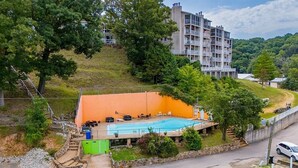 Edificio residencial con piscina, rodeado de árboles y una ladera.