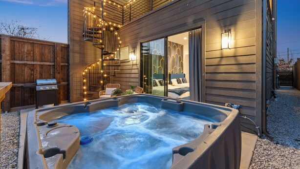 A hot tub in a backyard with a wooden fence, a grill, and string lights. - Luxe Loft with Hot Tub, Pool Table, Balcony, BBQ (Dallas)