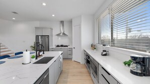A modern kitchen with white cabinetry, a large island, and a view of the outdoors through blinds. - Luxe Loft with Hot Tub, Pool Table, Balcony, BBQ (Dallas)