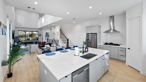 A modern kitchen with a large island, stainless steel appliances, and a staircase leading to a loft area. - Luxe Loft with Hot Tub, Pool Table, Balcony, BBQ (Dallas)