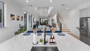 A modern kitchen with a central island, stainless steel appliances, and a dining area with blue chairs and a glass-top table. - Luxe Loft with Hot Tub, Pool Table, Balcony, BBQ (Dallas)