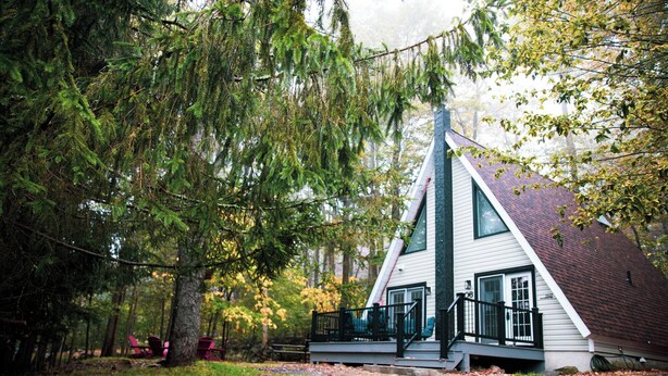 A cabin with a steeply pitched roof, a front porch, and a visible staircase leading to the entrance. - Cozy Poconos A-Frame Cabin with Fire Pit, Pool, Lake (Tobyhanna)