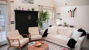 A living room with a black fireplace, a sofa, two armchairs, a coffee table, and a dining area with a table set for two. - Cozy Poconos A-Frame Cabin with Fire Pit, Pool, Lake (Tobyhanna)