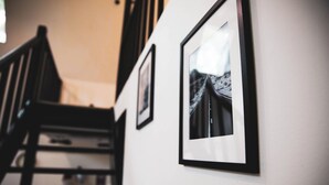A staircase with a wooden handrail and a white wall with framed pictures. - Cozy A-Frame Cabin, Fire Pit, Grill, Near Tobyhanna State Park (Tobyhanna)