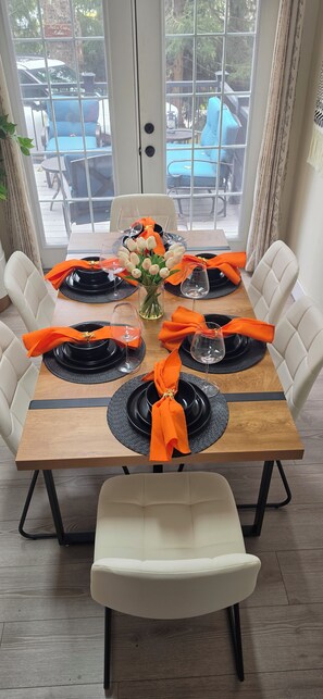 A dining table set for six with black plates, orange napkins, and a vase of white flowers. - A-Frame: Fire Pit, Deck, grill & Lake Community (Tobyhanna)