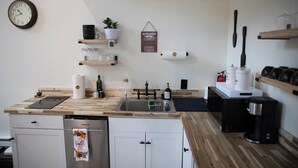 A compact kitchen with wooden countertops, a stainless steel sink, and a dishwasher. There are shelves with glassware and a sign that reads "KITCHEN." - Cozy Poconos A-Frame Cabin with Fire Pit, Pool, Lake (Tobyhanna)