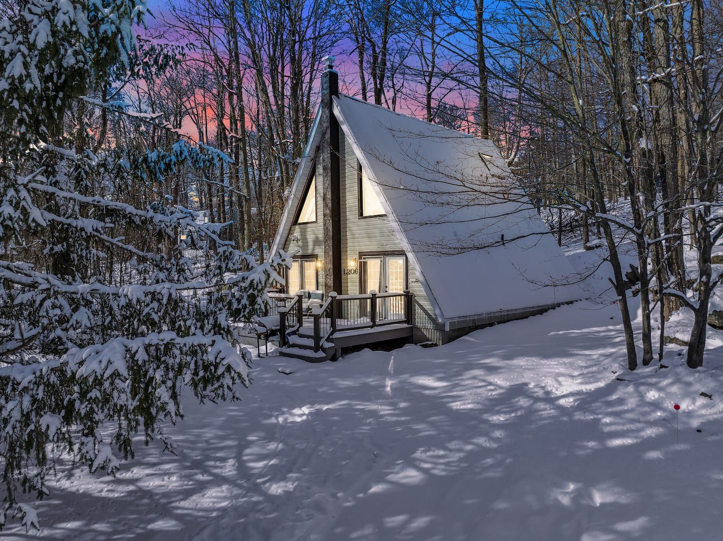 A cabin with a steep roof, surrounded by snow-covered trees.