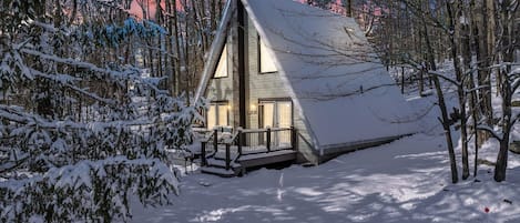 A cabin with a steep roof, surrounded by snow-covered trees.