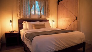 A neatly made bed with a wooden headboard, two bedside lamps, and a window with curtains. - Cozy Poconos A-Frame Cabin with Fire Pit, Pool, Lake (Tobyhanna)