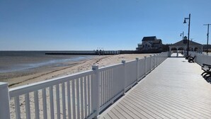 Een houten looppad dat naar een strand leidt, met een witte omheining en bankjes.