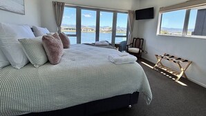 A bedroom with a large bed, a chair, and a view of the water. - Charming Lakeview Golf Villa (Matarangi)