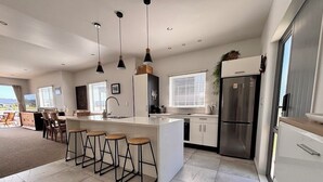 A modern kitchen with a central island, bar stools, stainless steel appliances, and a view to the outside. - Charming Lakeview Golf Villa (Matarangi)