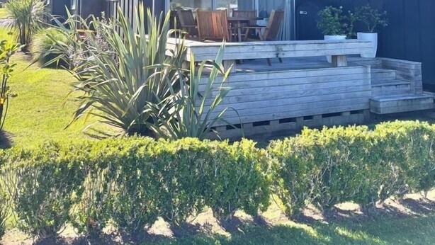 A modern two-story house with a balcony, a deck, and a well-maintained garden. - Charming Lakeview Golf Villa (Matarangi)