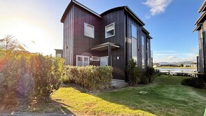 A modern two-story house with a dark exterior, a small front porch, and a well-maintained lawn. - Charming Lakeview Golf Villa (Matarangi)