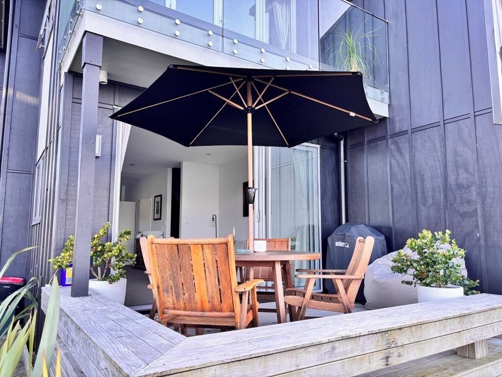 An outdoor patio with a table and chairs, a large umbrella, and potted plants.