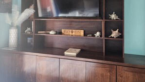 A wooden entertainment center with a flat-screen TV, decorative shells, and a sign reading "BEACH HOUSE". - Tranquil Paradise w/ private round-trip transportation and custom KING Beds, (BAY ISLANDS)