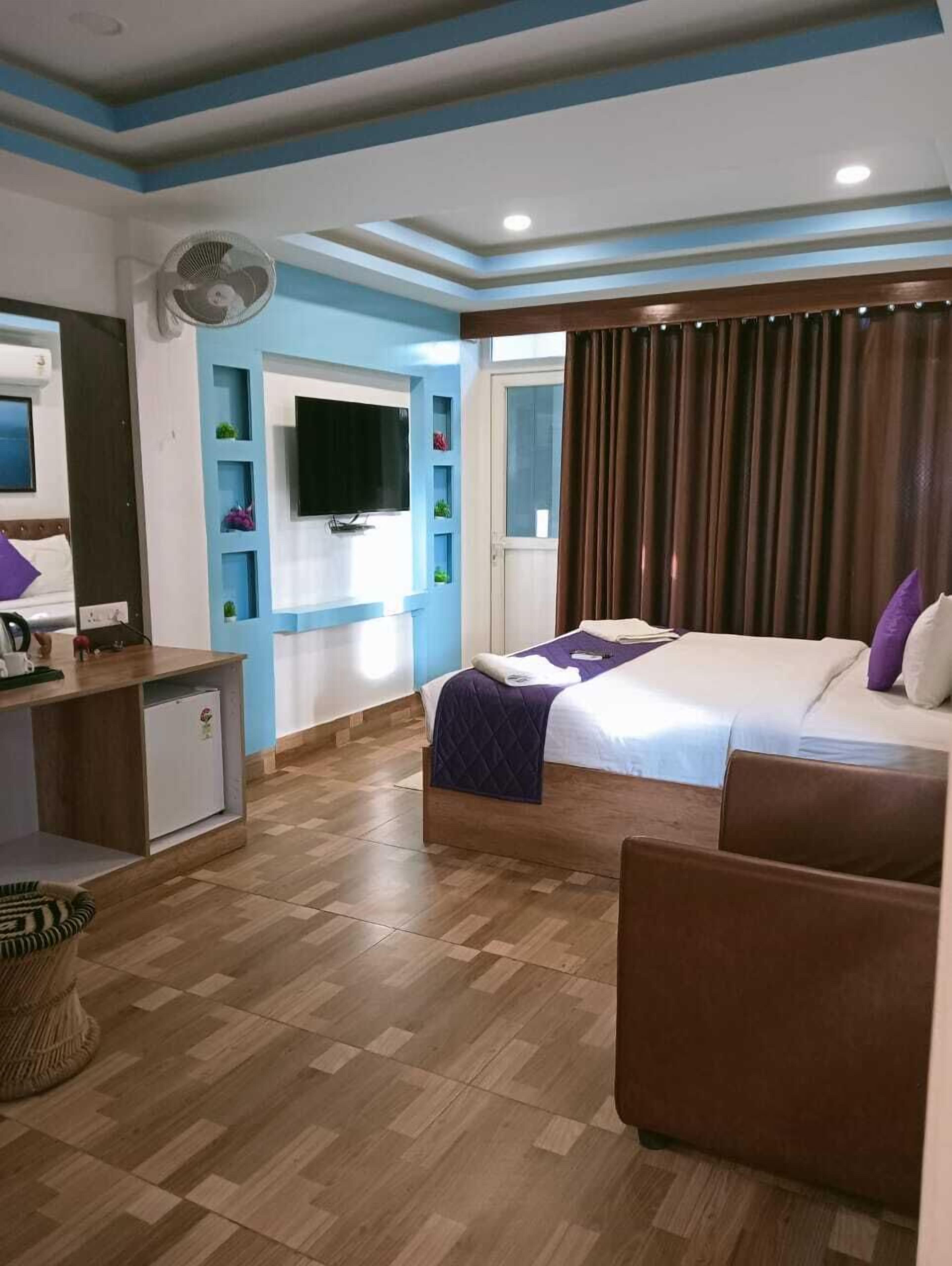 A hotel room with a bed, a desk, a television, and a fan.