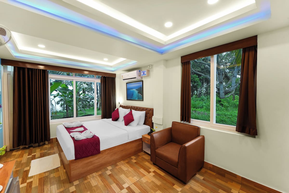 Una habitación de hotel con una cama, un sillón de cuero marrón, una mesita de noche y una ventana con vistas a zonas verdes.