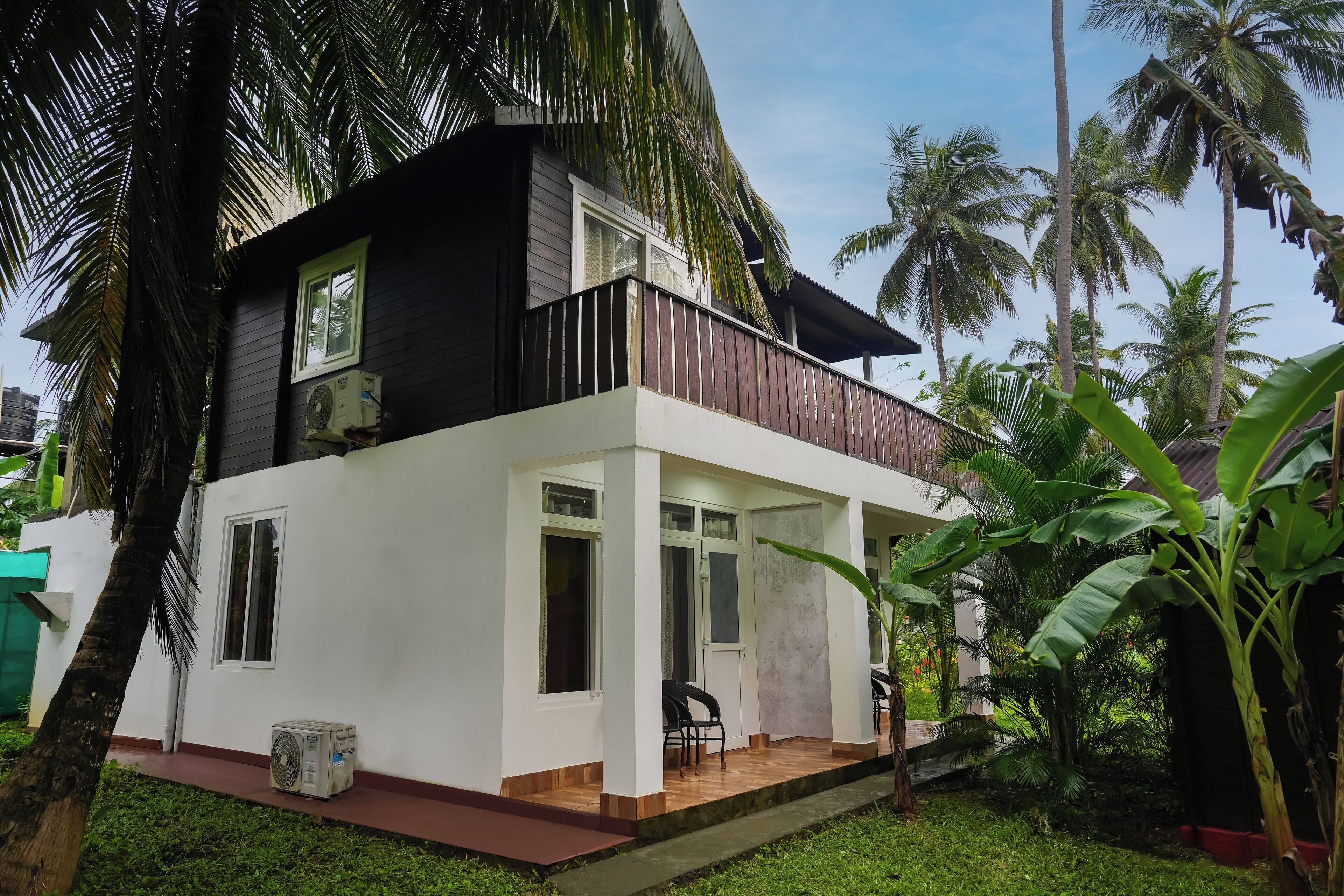 Uma casa de dois andares com varanda, rodeada por vegetação exuberante e palmeiras.