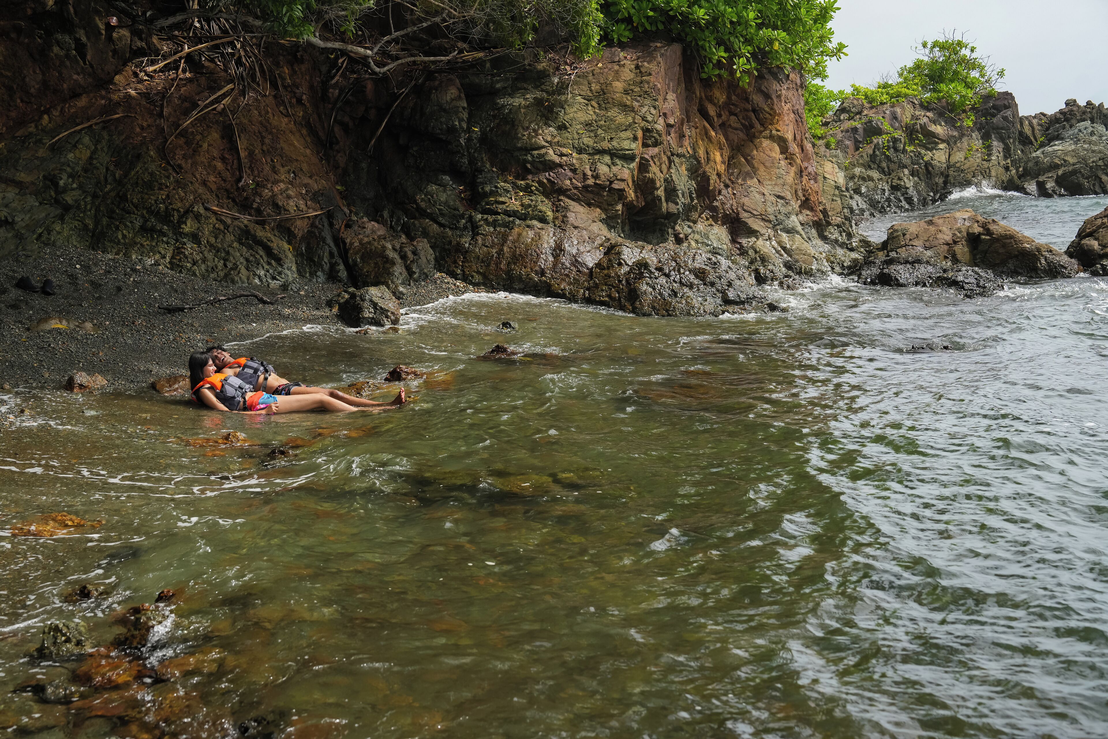A person lying on a rocky shore in a clear stream.