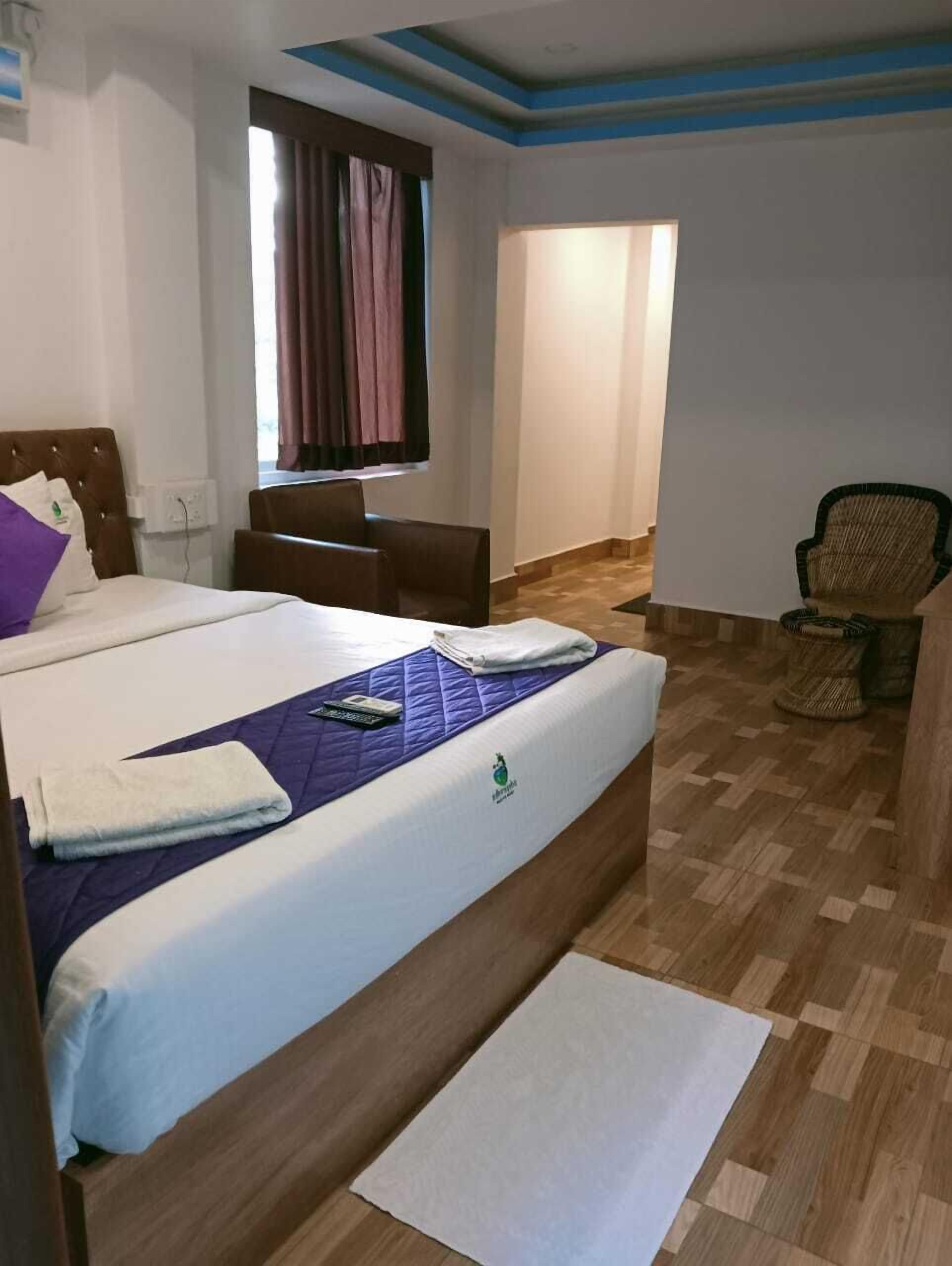 Quarto de hotel com cama, escrivaninha, cadeira e janela com cortinas.