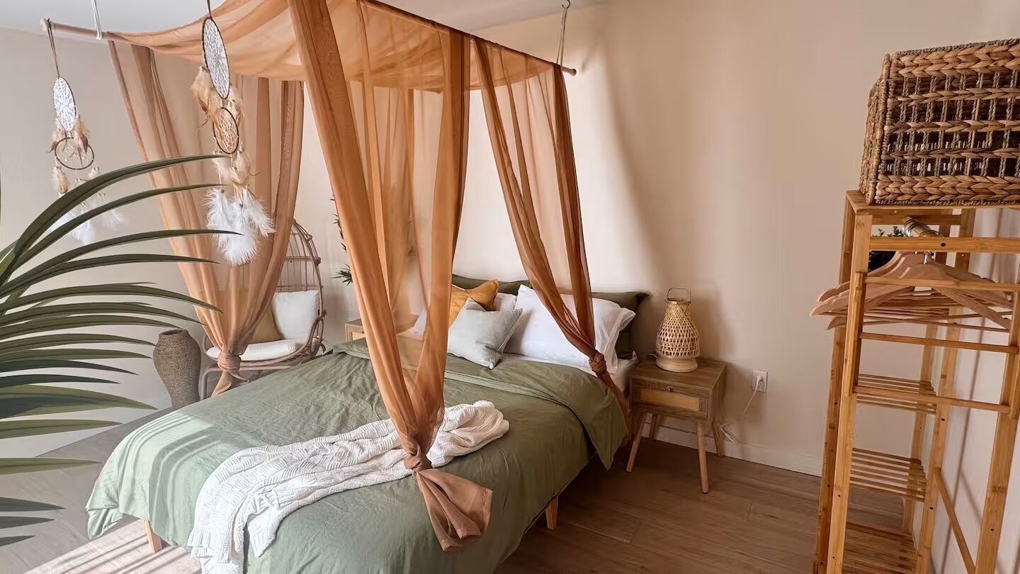 A bedroom with a canopy bed, bedside tables, a woven basket, and a large plant.