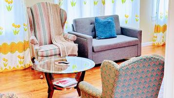 A living room with a striped armchair, a patterned armchair, a grey sofa with a blue pillow, and a glass coffee table.