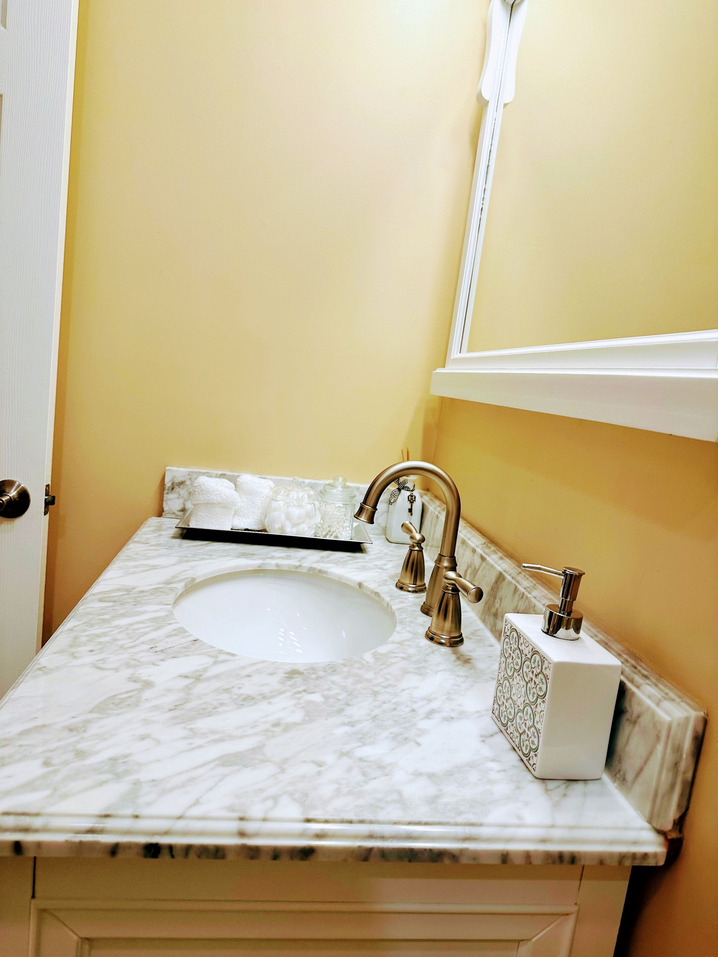 A bathroom with a marble sink, a gold faucet, and a white soap dispenser.