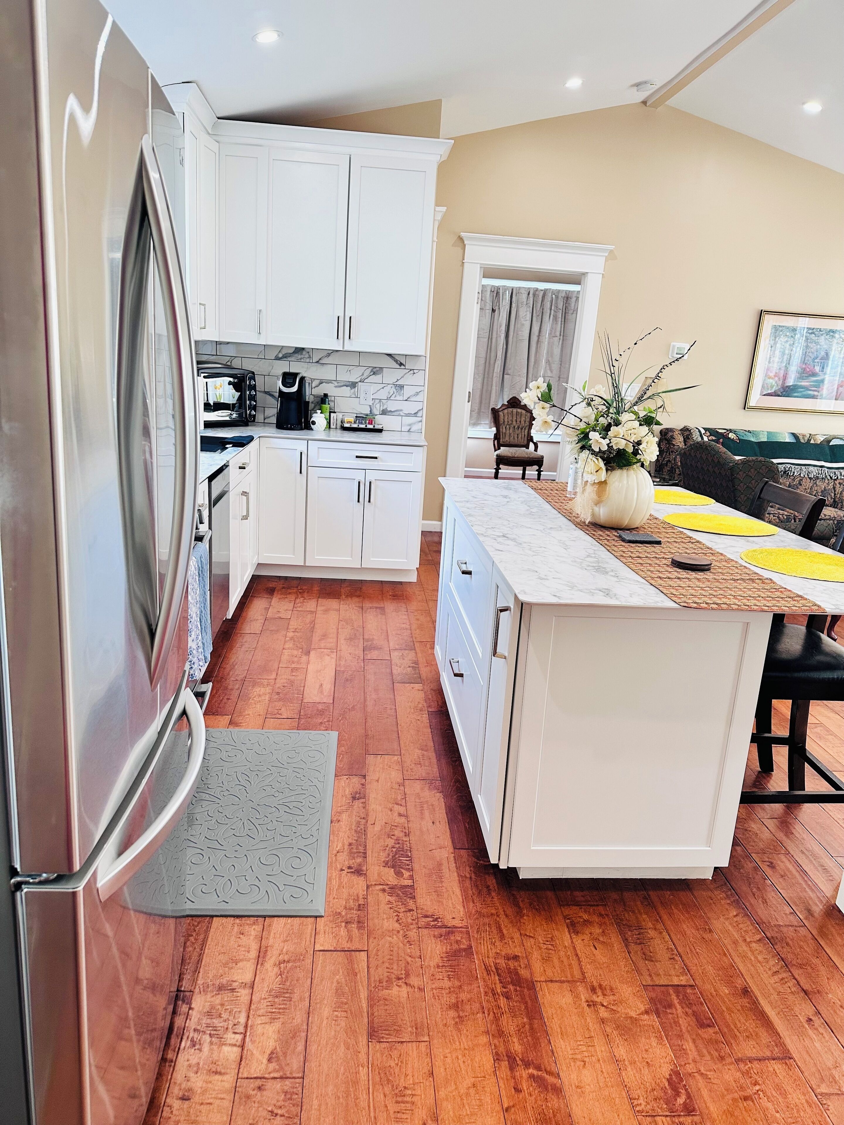 A modern kitchen with white cabinets, a marble countertop, and a wooden floor.