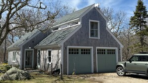 A two-story house with a garage, a sloped roof, and a small attached shed. - Newly Renovated Charming Guest House in Chilmark with WiFi, AC, Covered Porch (Chilmark)