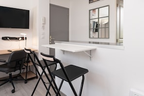Une pièce moderne équipée d’un bureau, de deux chaises noires, d’un téléviseur fixé au mur, d’une porte et d’un miroir.