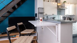 Eine moderne Küche mit weißen Schränken, einem schwarzen Stuhl, einem weißen Tisch und einer blauen Wand.