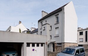 Um edifício residencial com garagem, um carro estacionado na frente e céu claro.