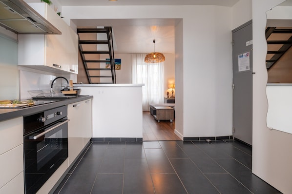 Une cuisine moderne dotée d’un four encastré, d’un plan de travail noir et d’un escalier menant à un espace repas.