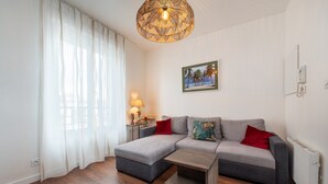 Ein modernes Wohnzimmer mit einer Eckcouch, einem kleinen Tisch, einer Lampe und einem gerahmten Bild an der Wand.