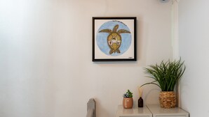 Ein gerahmtes Kunstwerk mit einer Schildkröte an der Wand, ein Blumentopf und eine kleine Vase mit Schilf auf einem Nachttisch.