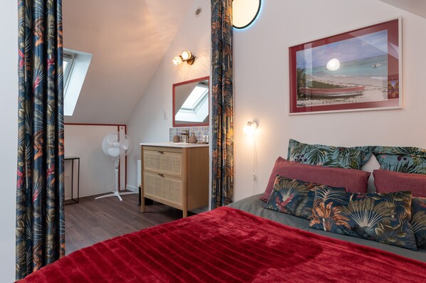 A bedroom with a bed, a dresser, a fan, a window, and a painting on the wall.
