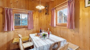 Un interior de fusta amb taula de dinar, cadires, un penjallum i cortines a quadres.