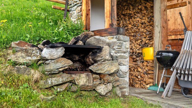 Una cabana rústica amb paret de pedra, porta de fusta i una barbacoa a l'exterior.