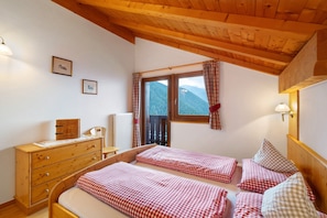 Ein Schlafzimmer mit zwei Betten, Holzmöbeln, einem Fenster mit Vorhängen und gerahmten Bildern an der Wand.