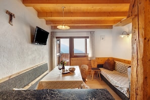 Una habitación acogedora con techo de madera, un televisor montado en la pared, una mesa de comedor con mantel blanco, un sofá y una ventana con vistas.