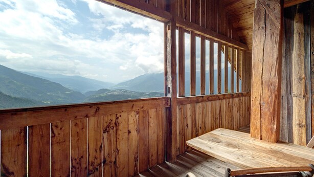 Une cabane en bois avec une table et un banc en bois, de grandes fenêtres offrant une vue sur les montagnes.