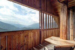Eine Holzhütte mit Holztisch und Bank, große Fenster mit Blick auf die Berge.