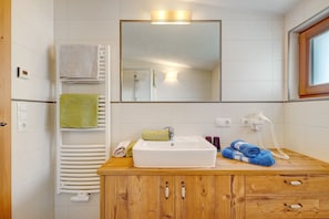 Un baño con tocador de madera, un lavabo blanco, un espejo, un perchero para toallas y un teléfono.