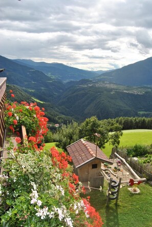A rural house with a small garden, surrounded by mountains and greenery.