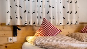A wooden bed with checkered bedding, a red and white checkered pillow, and a wall-mounted light fixture.