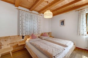 Et værelse med to senge, træhovedgærder, en bænk, en hængende lampe og et vindue med gardiner.