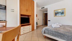 A hotel room with a bed, a TV, a wooden wardrobe, a desk, and a painting on the wall.
